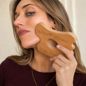 Woman using Qi Flow™ Activator wooden gua sha tool on cheek and jaw for facial massage