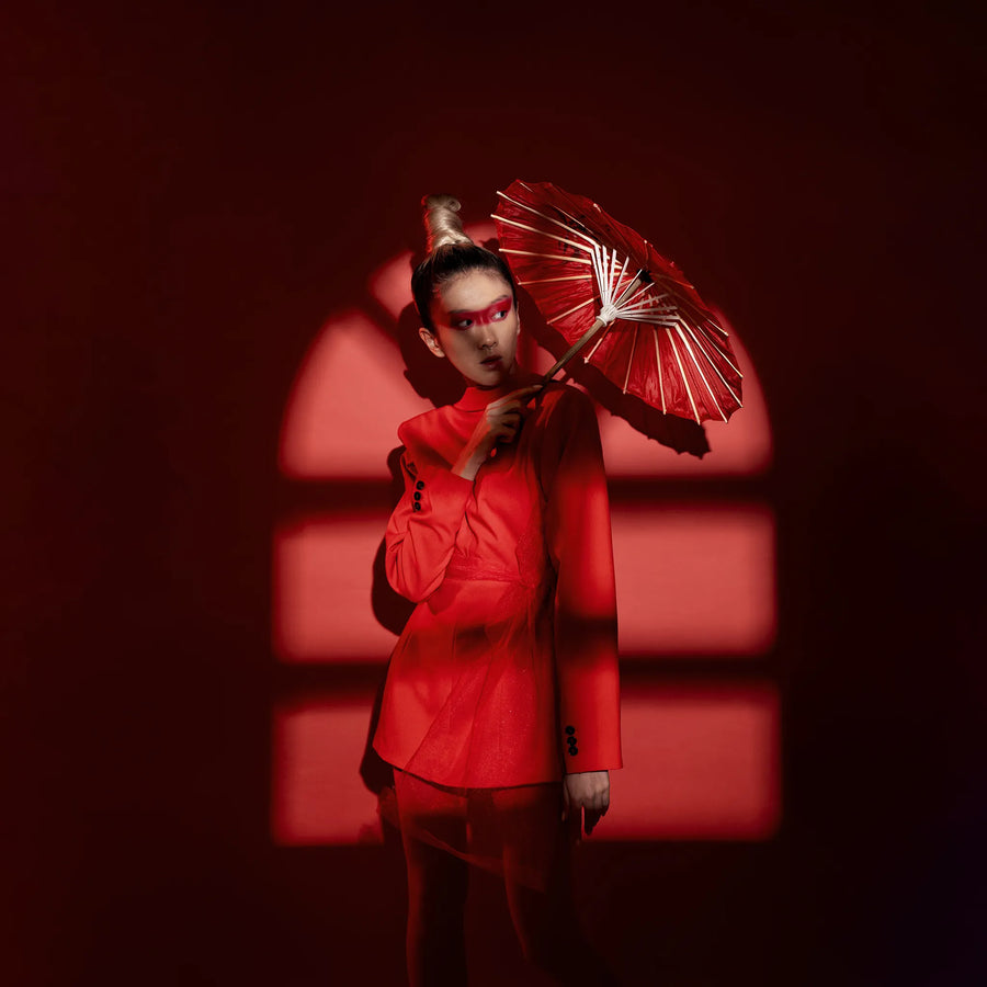 Woman holding a red parasol against a dark backdrop—symbolizing balance and tradition in Xian Rituals’ holistic wellness approach